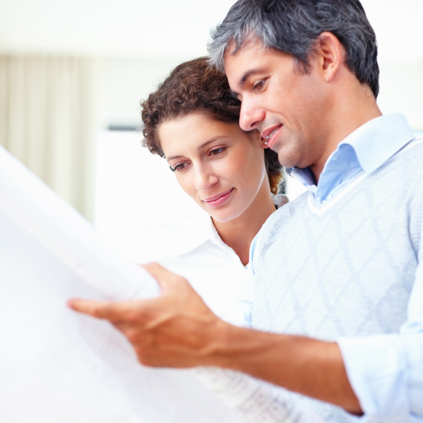 A man and a woman, interior design colleagues, are looking at architectural drawings together, with the man pointing at something on the page.