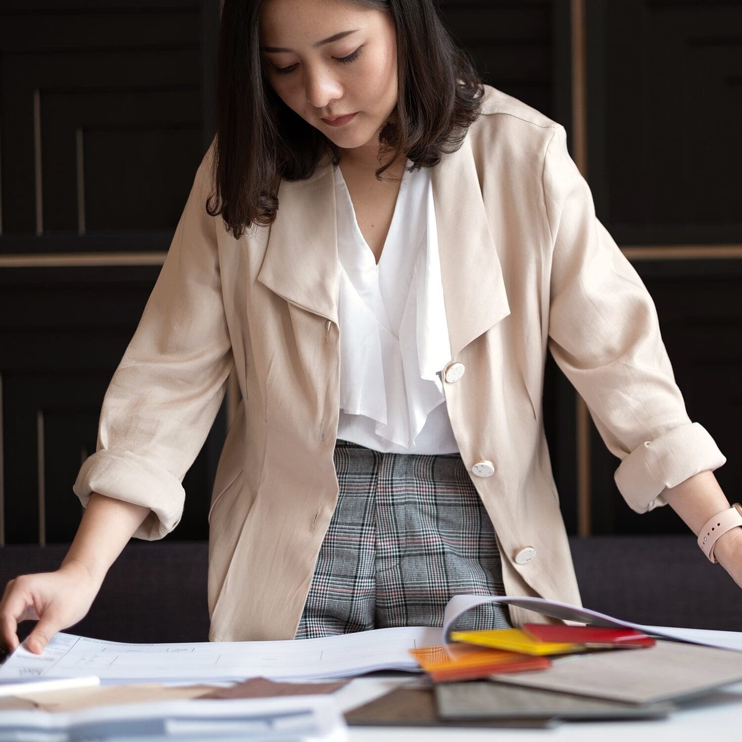 A female interior designer looking at a drawing package on a table surrounded by material samples.