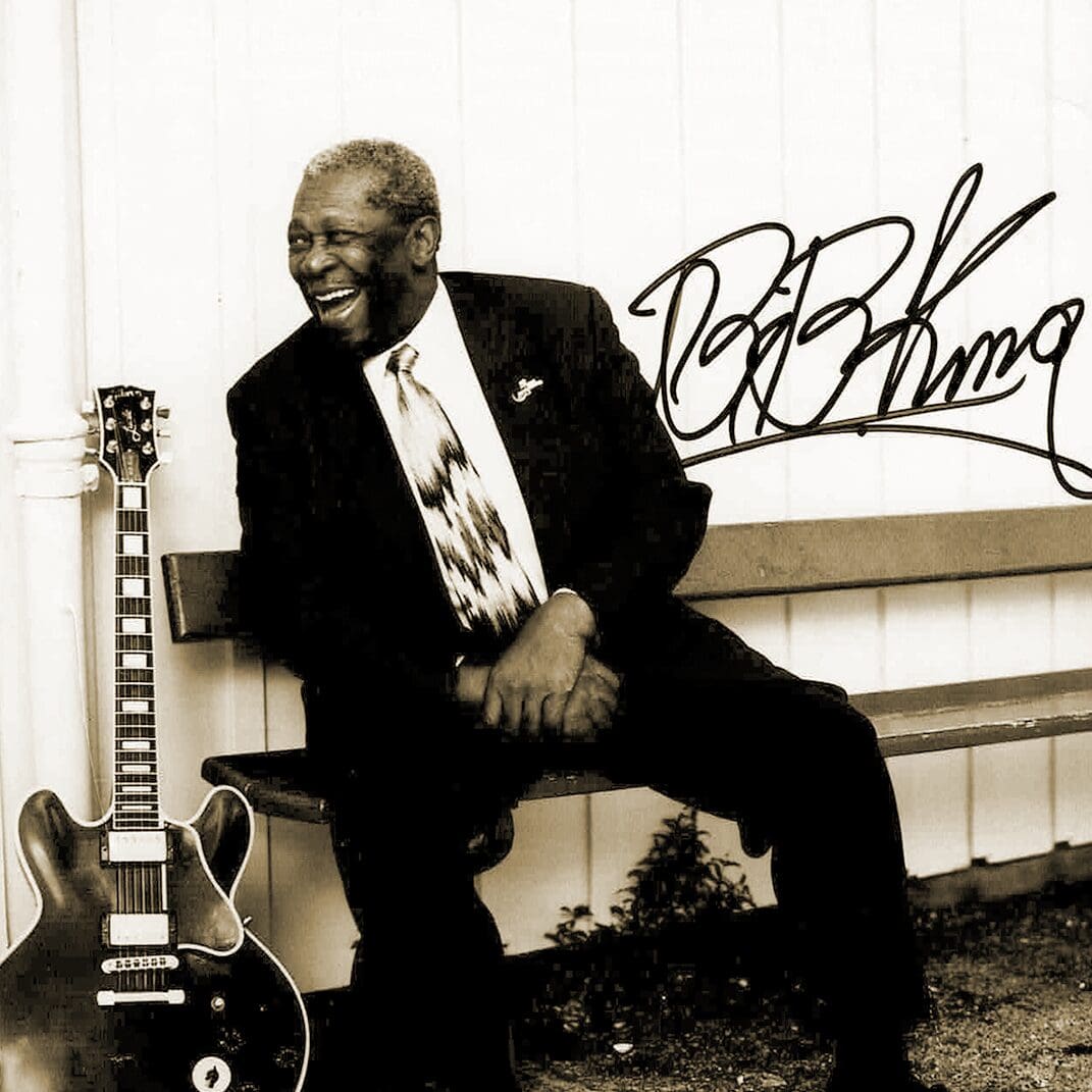 Autographed photo of B.B. King sitting on a bench with his guitar next to him.